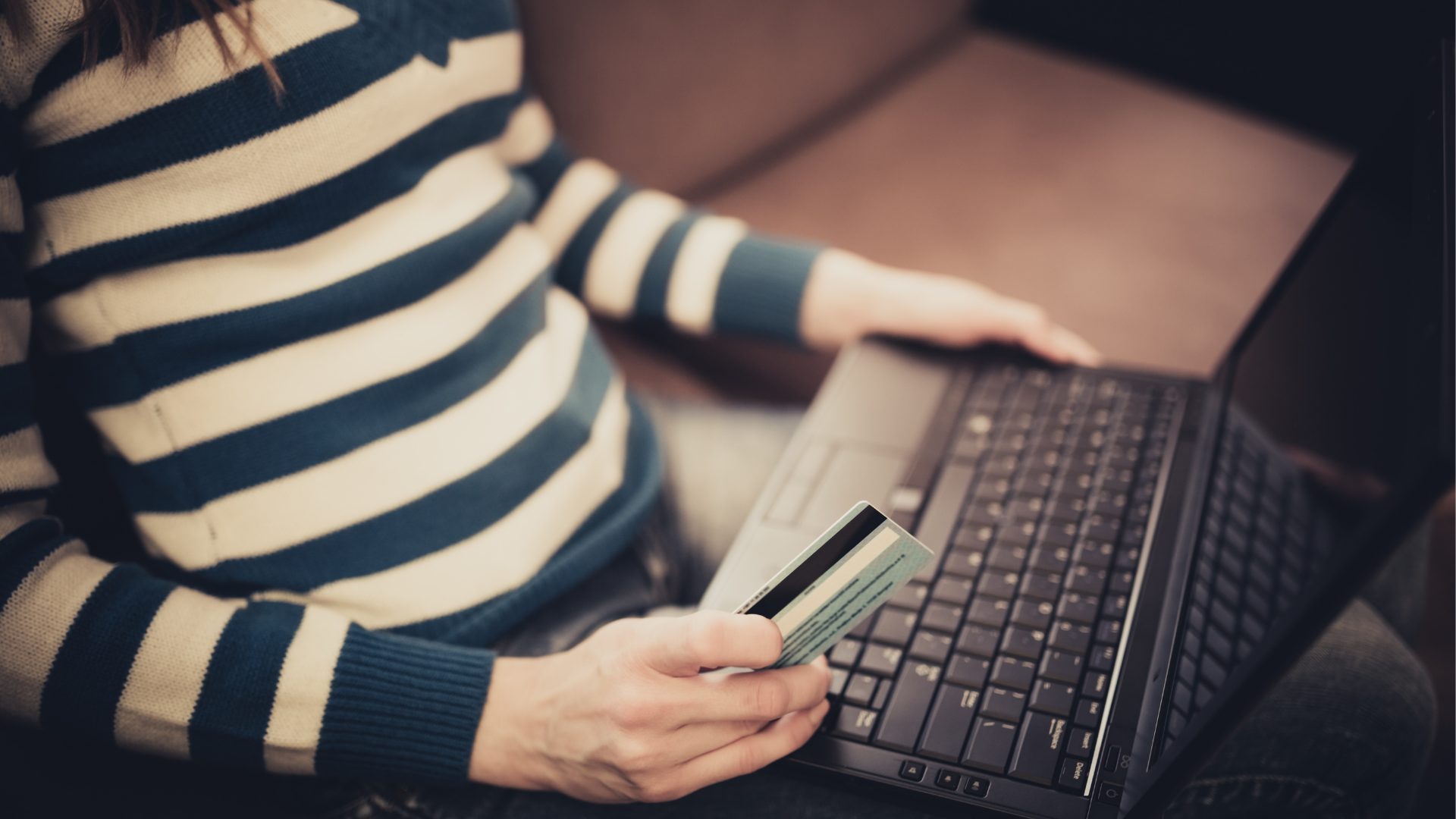 A person wearing a striped sweater making an online payment with a credit card. 