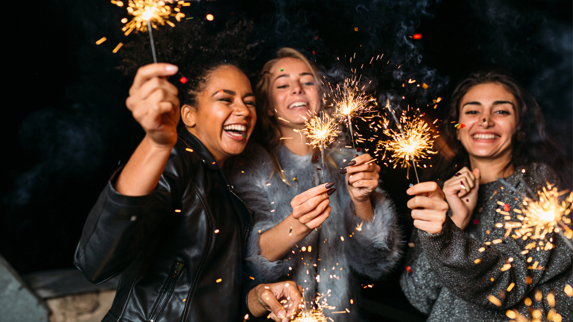 Three people celebrating at night with sparklers.