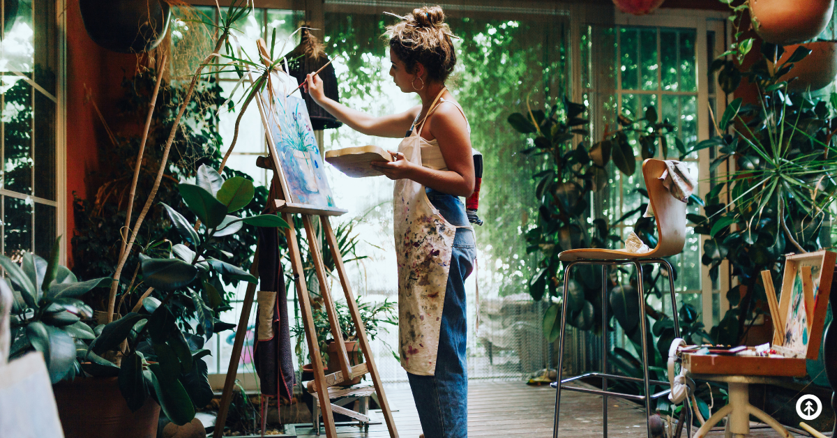 An artist using an easel to create a graphic design on canvas in a home office with plants.