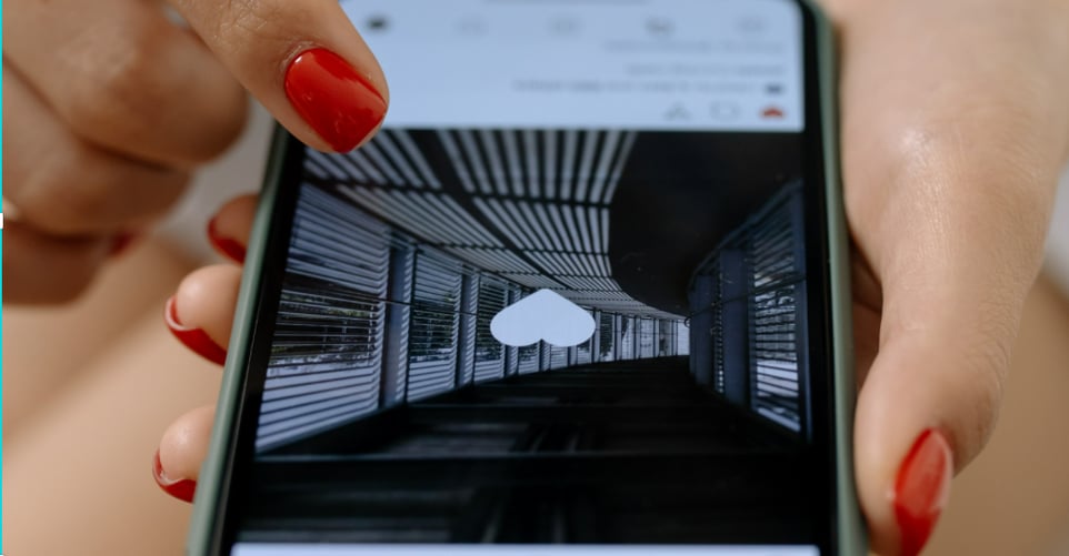 An image of a woman’s hand holding an iPhone that’s open to the Instagram screen with a liked black and white photograph of a winding hallway. 